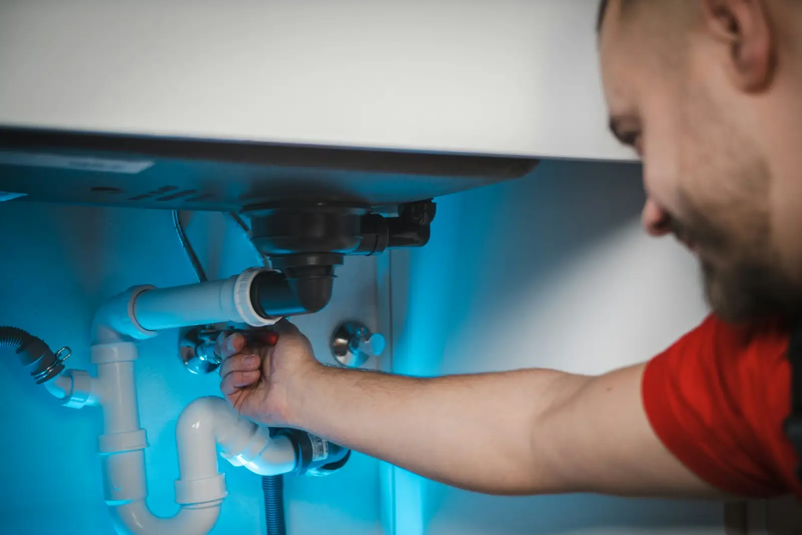 Plumber fitting a waste trap beneath a basin